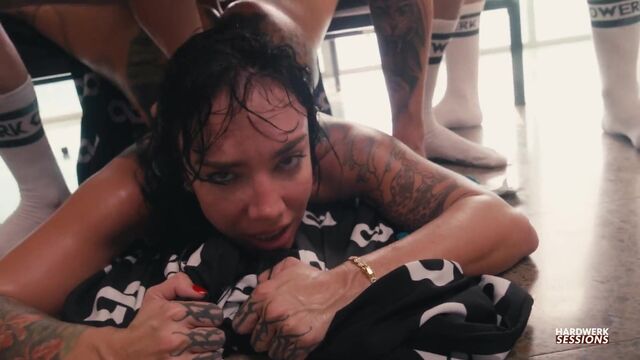 Her huge back tattoo flexes as she bends over between men in white socks